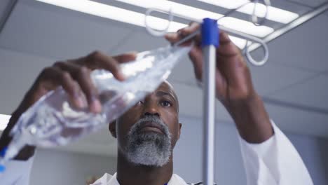 Médico-Afroamericano-Preparando-Una-Bolsa-De-Goteo-Para-Un-Paciente-En-La-Habitación-Del-Hospital