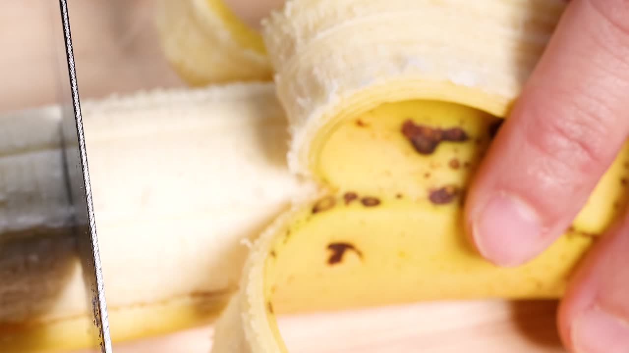 A detailed view of a banana being sliced with a knife, showing the texture and peel.
