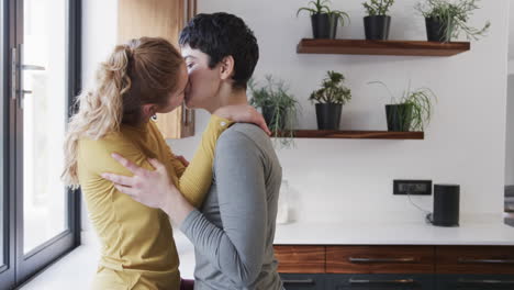 feliz pareja de lesbianas caucásicas abrazándose y besándose en la cocina soleada, copia el espacio