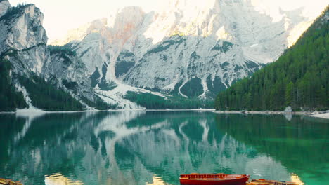 Flying-out-over-the-calm-emerald-green-waters-of-Lake-Braies,-revealing-the-Prags-Dolomites,-aerial