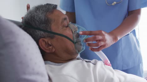 mixed race female doctor assisting senior man in bed at home using ventilator