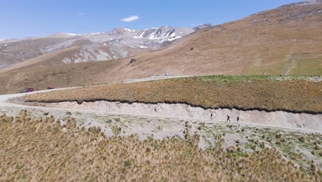three hikers on side of a dry mountain with snowy peak