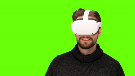 close up of man in latest modern white oculus quest 2 vr ar headset playing with mixed augmented reality controls swiping around green screen chroma keying futuristic communications experience happy