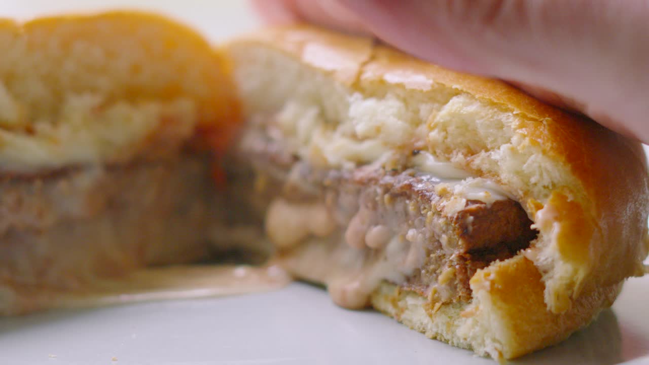 Gooey Cheese Oozing from Middle of Burger as Hand Presses Down on Bun in Slow Motion. Example of Unhealthy but Delicious Fast Food.
