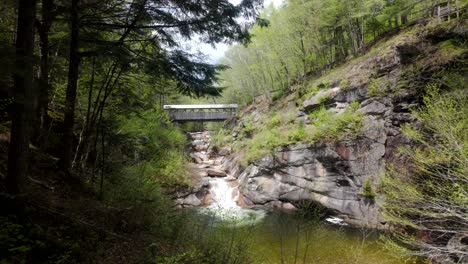 A wide view of Flume Gorge covered bridge spanning rocky stream and forest trail, establishing static