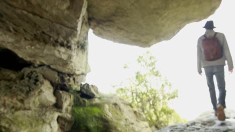 excursionista masculino de pie con una mochila cerca de una cueva 4k