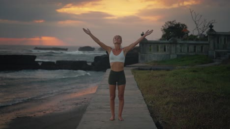 woman practicing sun salutation asana yoga pose outside during moody sunset