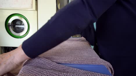 older female ironing a folded shirt garment at a laundromat store, locked tripod shot