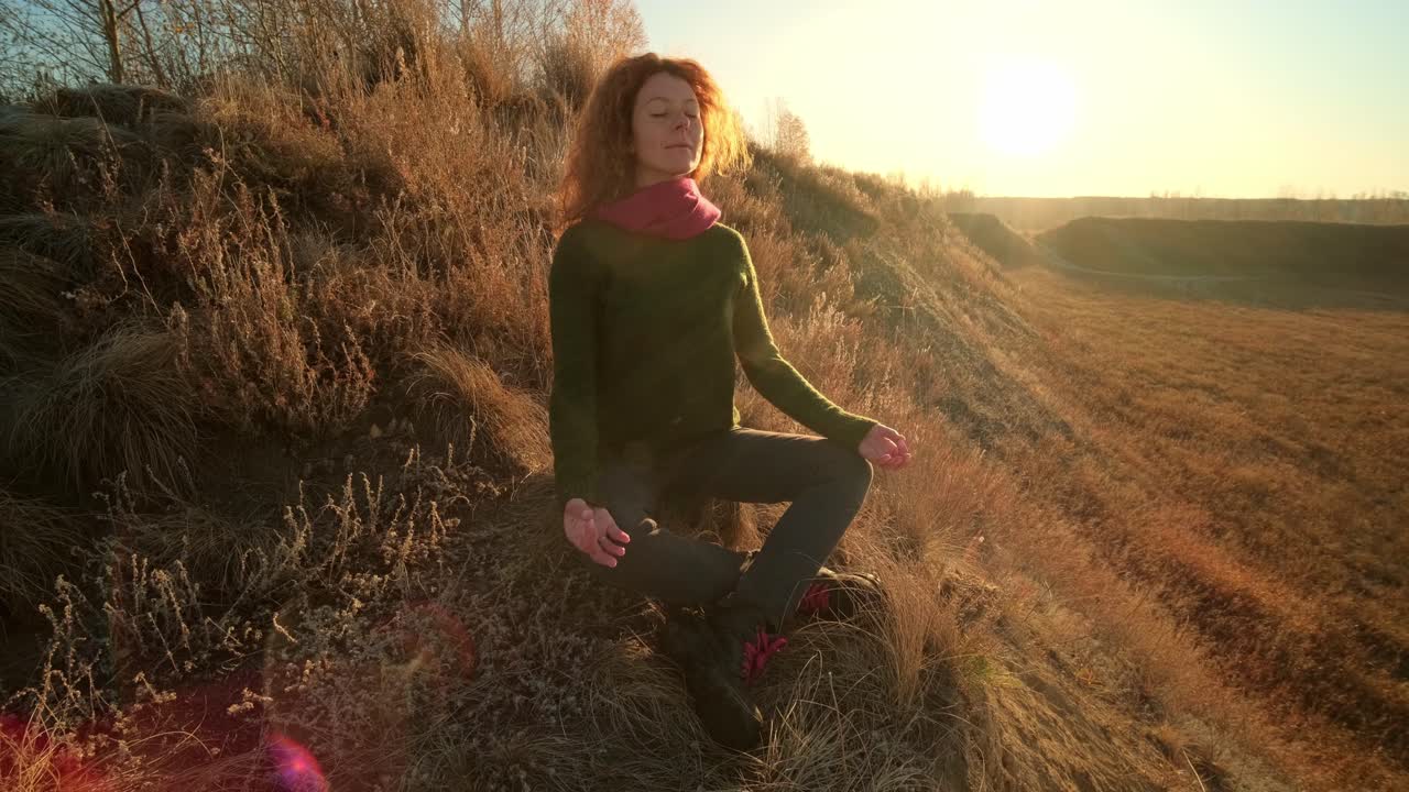 Woman meditating in a field at sunrise/sunset