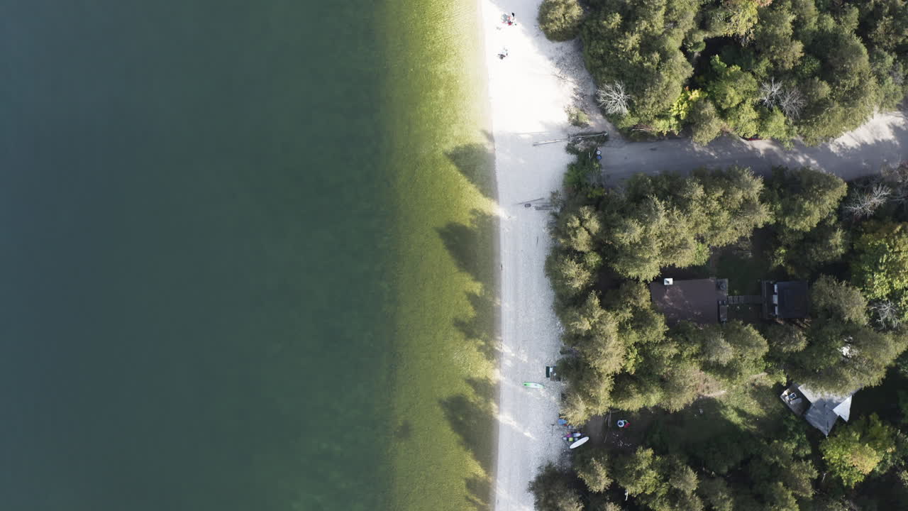 From above, the gentle gradient of Pebble Beach’s emerald shallows meets a sunlit road bordered by dense forest, capturing the serene transition between land and water in Door County