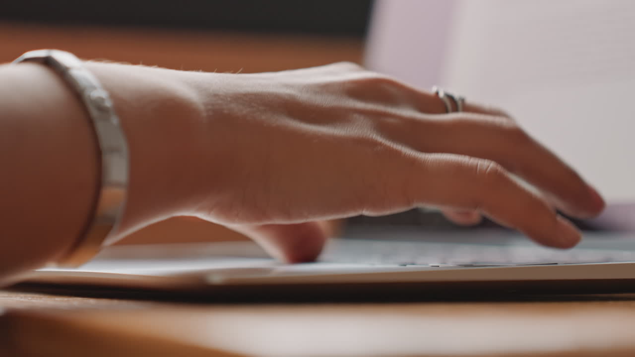 Hotel guest typing on laptop, closeup of hands and fingers on keyboard with document on screen, warm morning sunlight on wooden desk, visible bracelet and ring, focused atmosphere of remote work