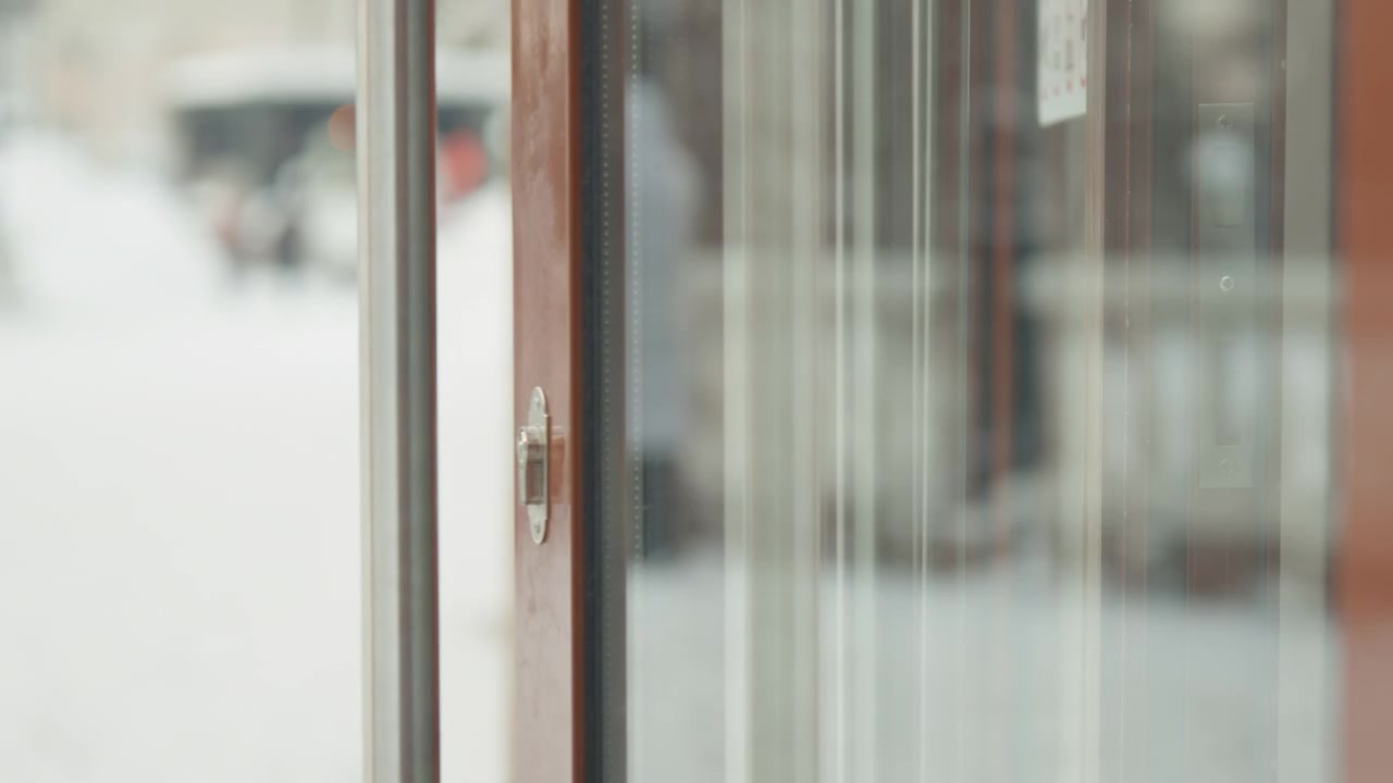 Tight vertical view of multiple glass doors and window panes with metal frames and visible latch hardware, shallow depth of field keeping middle frame sharp while foreground and background blur