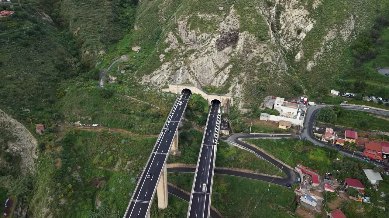 Drone tilt down along elevated highway into tunnel, stretching between steep slopes near Taormina