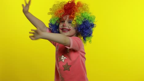 little child girl clown in colorful wig making silly faces, shouts, grabs her head, waves her hands