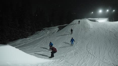 4k slow motion of group of skiers and snowboard jumping on medium sized snow hill in fun park at night in ski resort in norway