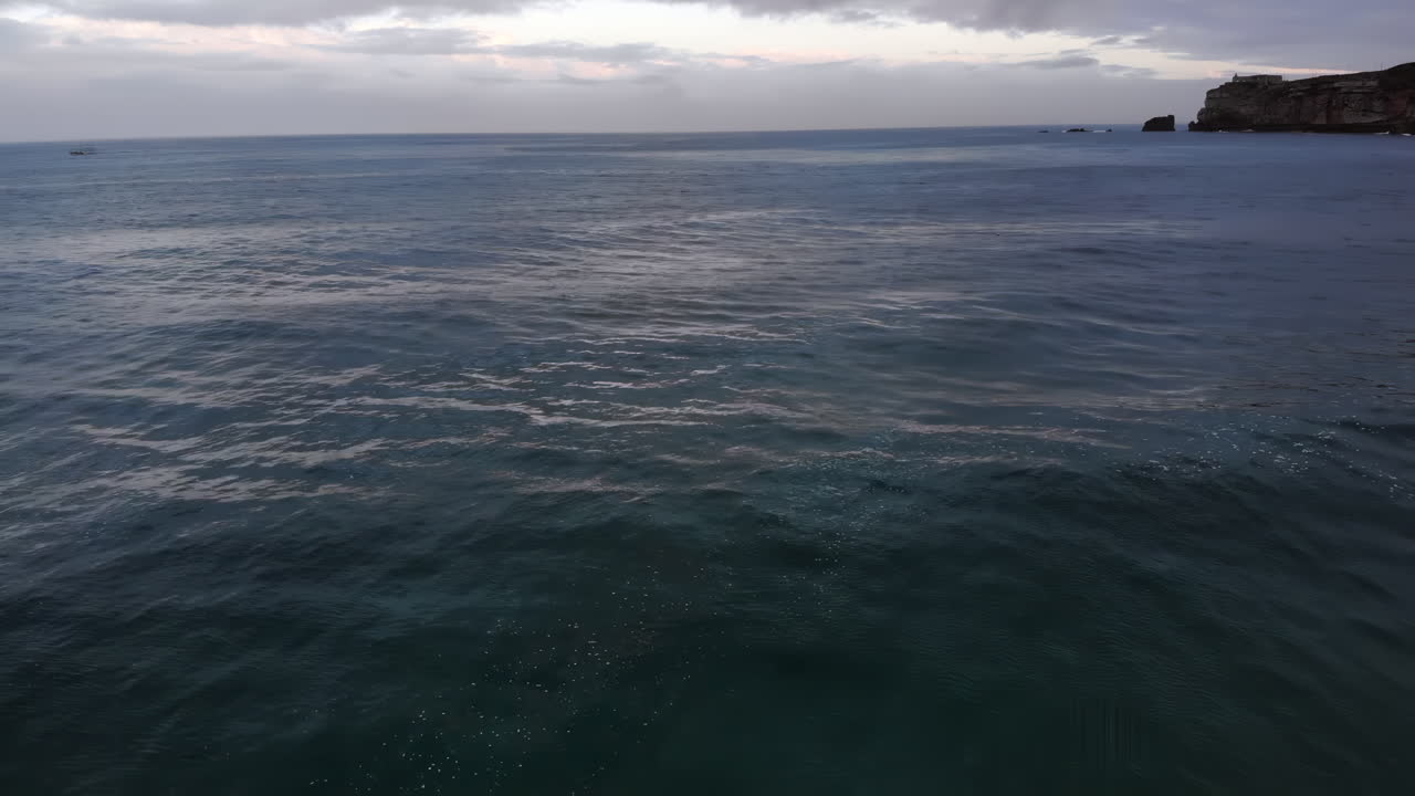 Le onde delicate si infrangono dolcemente sulla spiaggia sabbiosa mentre il sole tramonta sullo sfondo. L'atmosfera tranquilla offre un momento perfetto di relax e bellezza in riva all'oceano.