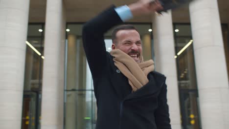 excited businessman gesturing yes holding briefcase outdoor against modern office building