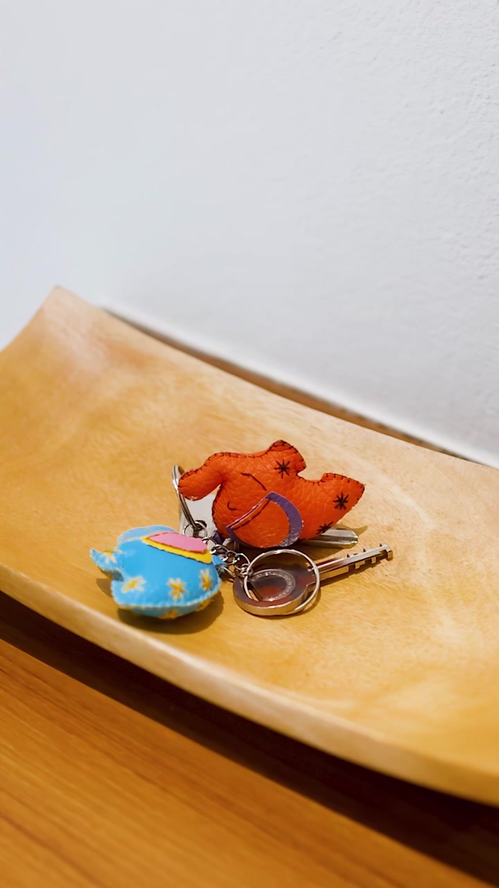 Static close-up of a hand setting house keys down on a curved wooden tray