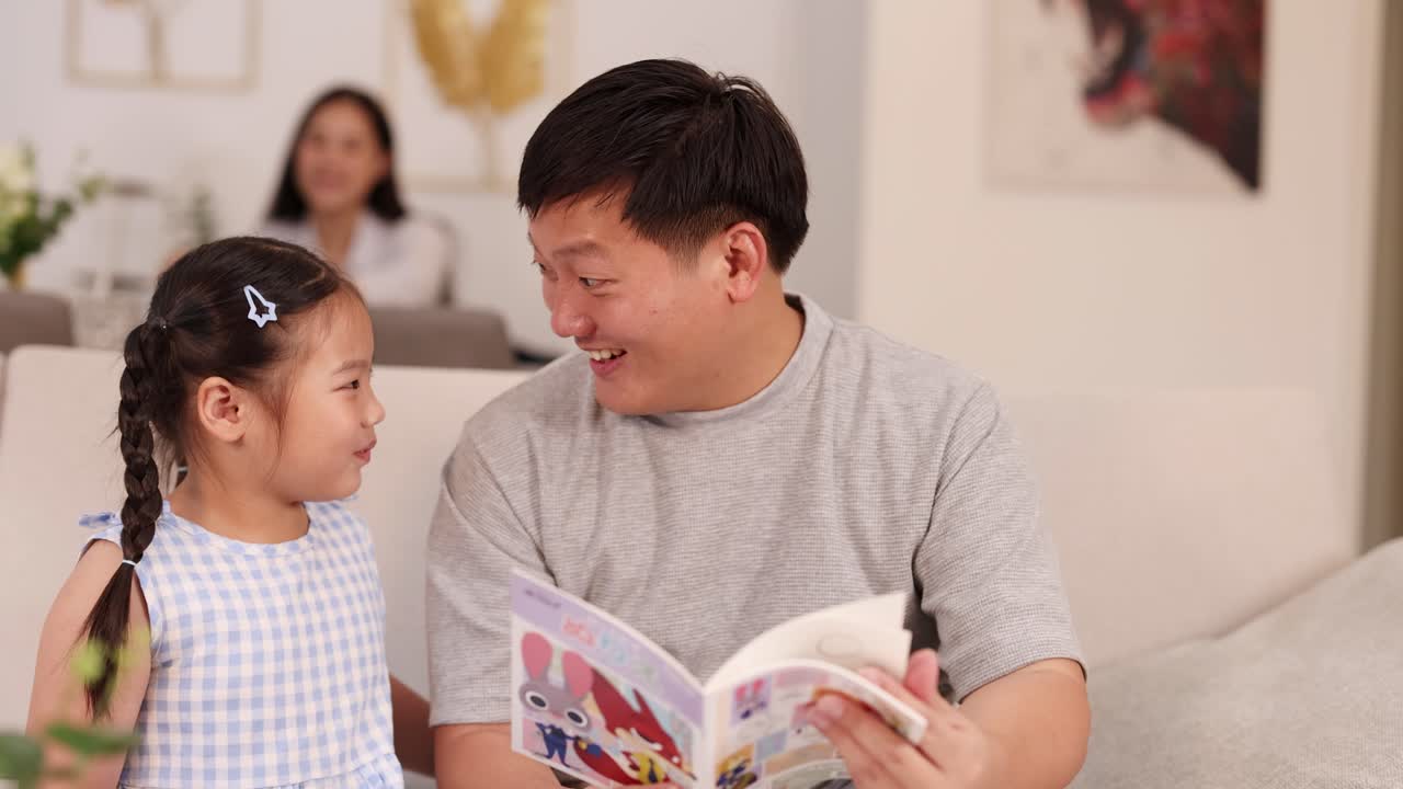 Father and daughter share a joyful reading moment on a sofa, with warm lighting and a relaxed atmosphere