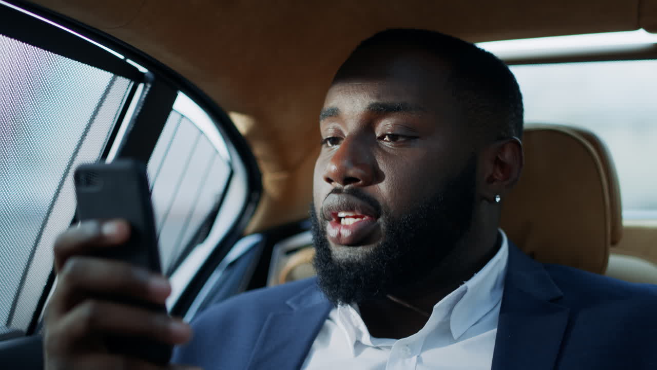 자동차에서 스마트폰을 사용하는 아프리카 사업가. 화가 난 아프리카 남자가 눈을 문지르고 있다.