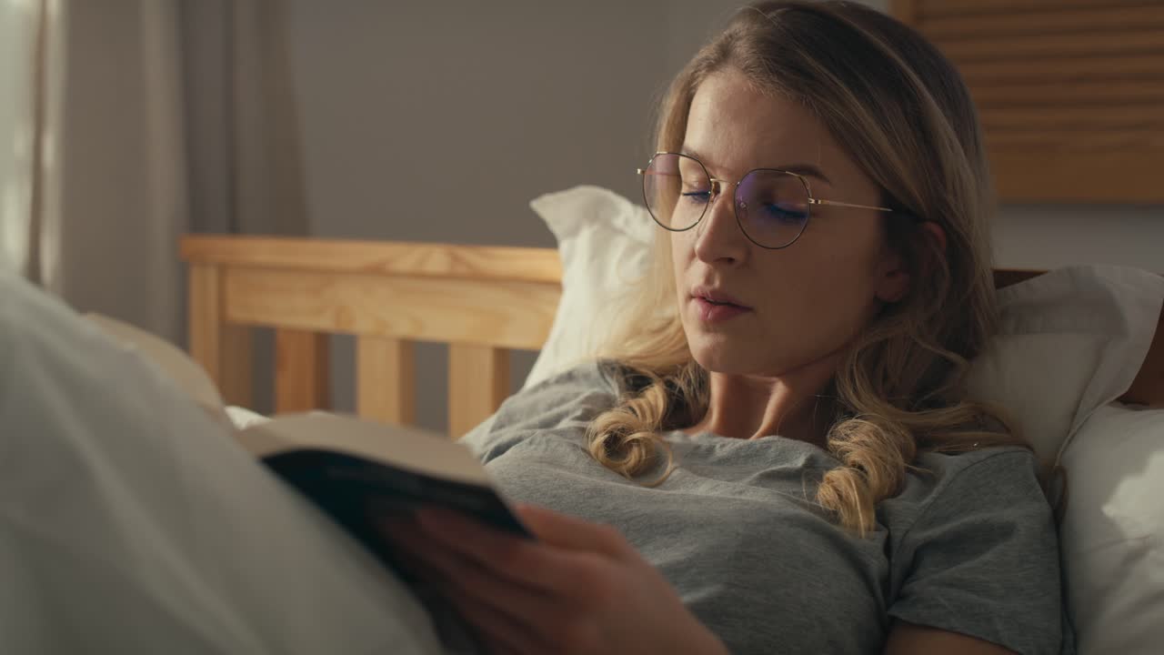 Caucasian woman lying down in bed and reading book at the morning.