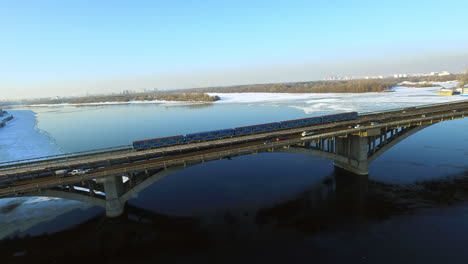 drone view etro train riding on bridge railway at winter. car traffic on highway