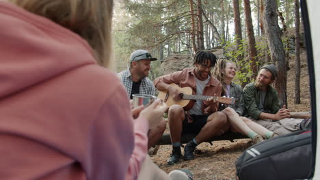 friends playing guitar in forest camping trip