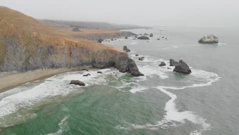 expansive aerial pan out of a surfer waiting to ride the waves along the sonoma coast