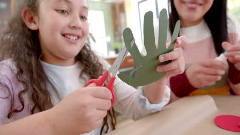 Happy-biracial-mother-and-daughter-cutting-cutouts,-talking-and-smiling-in-sunny-living-room