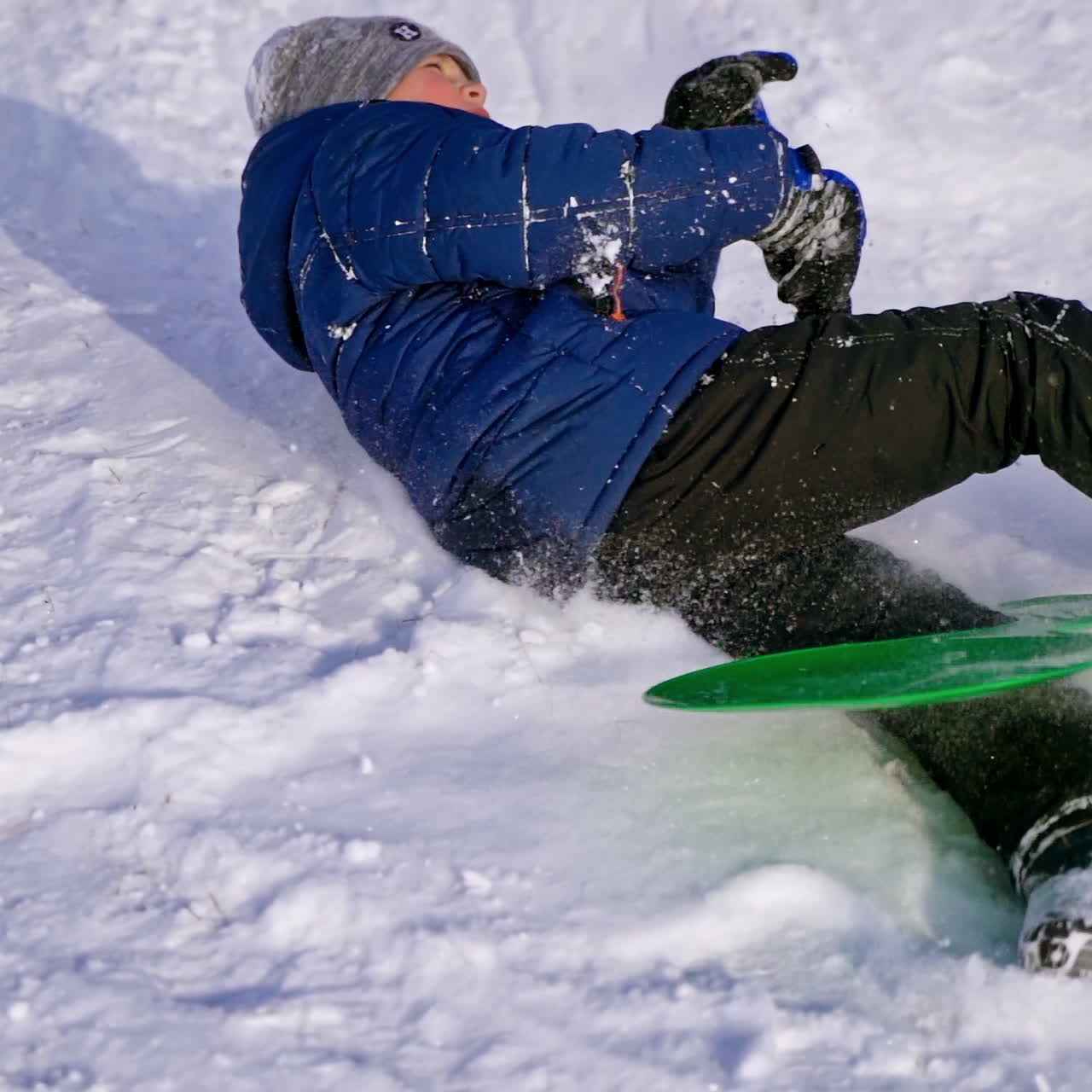 View from below on a boy sledding. Cute child riding from snow slide in winter. Cheerful vacation. Slow motion.