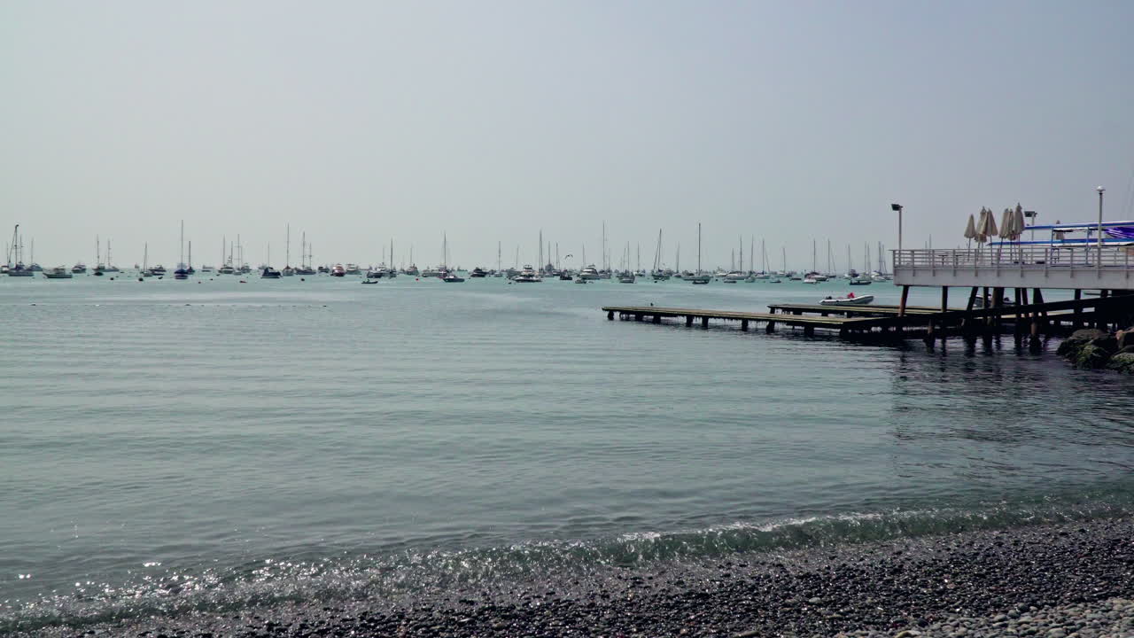 tiro estático del muelle de madera a lo largo de la costa con veleros atracados en la distancia en la punta, callao, perú en un día soleado