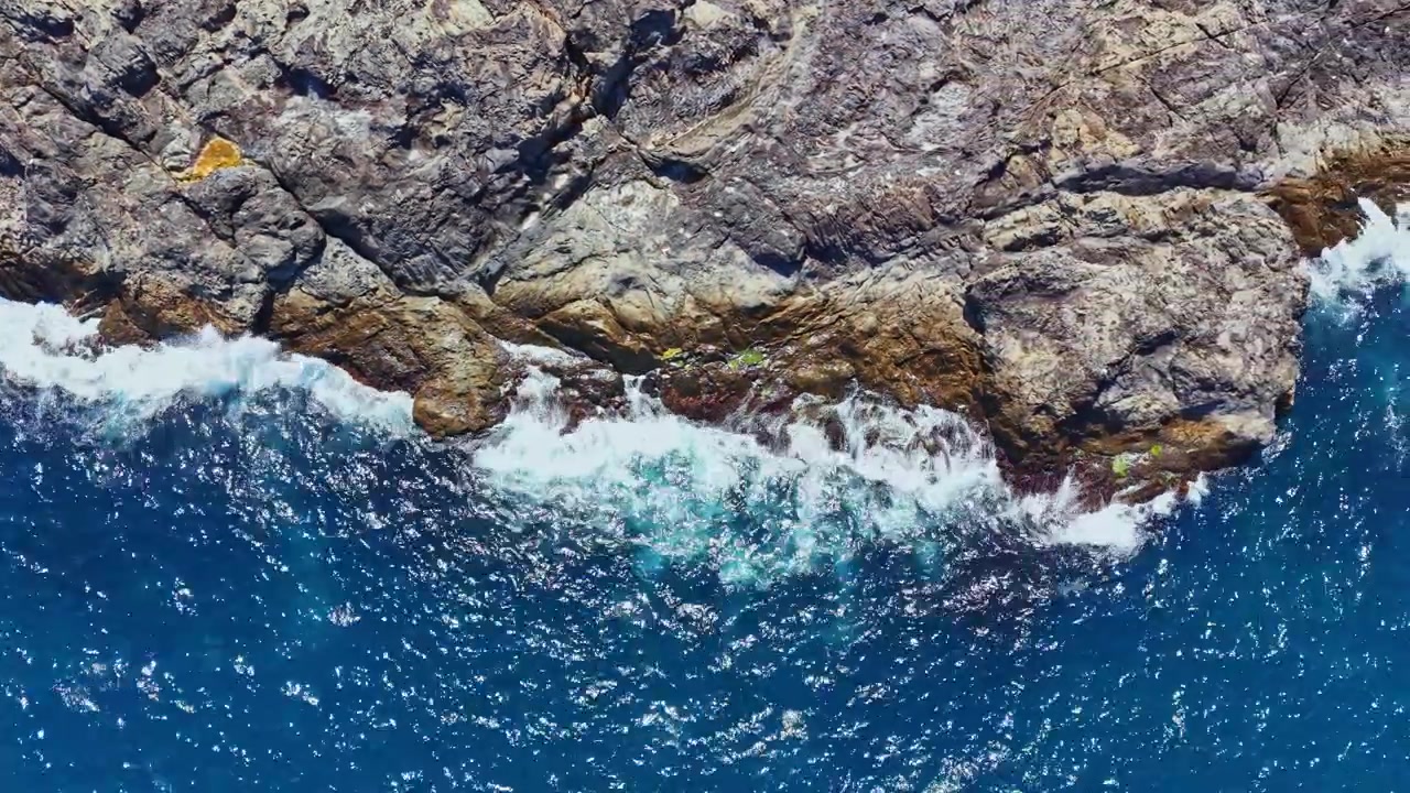 Rocce e onde si incontrano sulla riva dell'oceano in una giornata di sole.