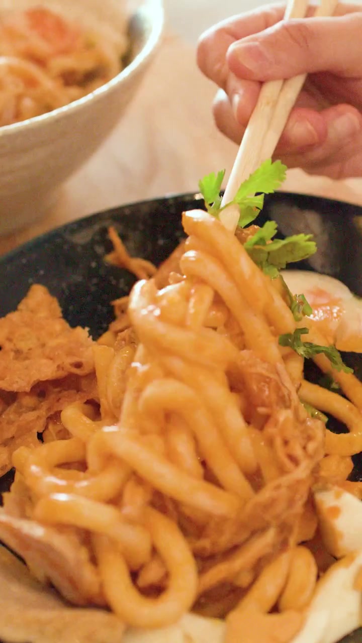 Primo piano di mani che mescolano spaghetti di riso spessi con pollo e uovo usando le bacchette a Bangkok
