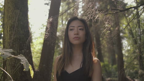 closeup of asian woman in black looking forward and exploring sunny forest, slowmo