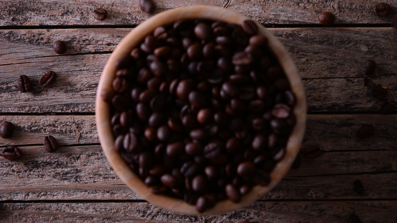 Chicchi di caffè tostati che cadono in una ciotola di legno