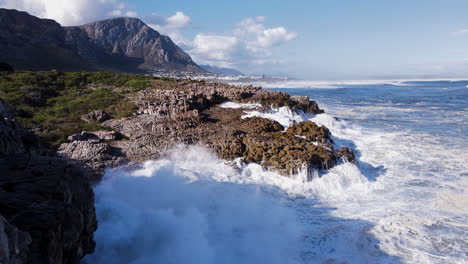 Drone-view-of-waves-thrashing-rocky-coastline,-Sieverspoint,-Hermanus