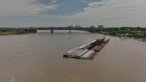 memphis tennessee antena v53 sobrevuelo inverso capturando un remolcador empujando una barcaza de tolva derramada en la vía fluvial del río mississippi con puentes y vista del paisaje urbano - filmada con cine mavic 3 - mayo de 2022