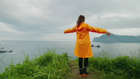 woman in orange rain gear on a cliffside overlooking the ocean