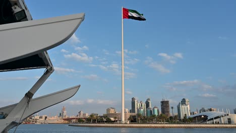 Bandera-De-Los-Emiratos-árabes-Unidos-Ondeando-En-El-Aire-Cielo-Azul-Nublado-En-El-Fondo,-Isla-De-La-Bandera-De-Sharjah,-Ciudad-De-Sharjah,-Día-Nacional-De-Los-Emiratos-árabes-Unidos,-Video-De-4k