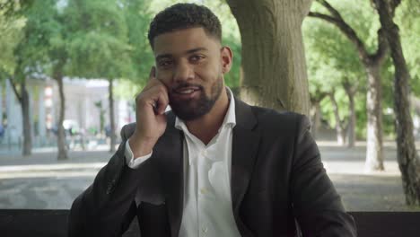 hombre de negocios sonriente hablando por teléfono inteligente en el parque.