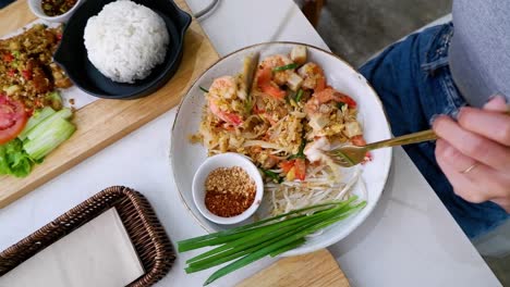 person eating prawn pad thai with side dishes
