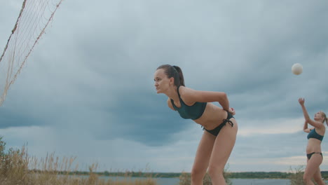 serve and attack in beach volleyball match of two ladies teams on open sandy court at summer cloudy day slow motion shot championship and training