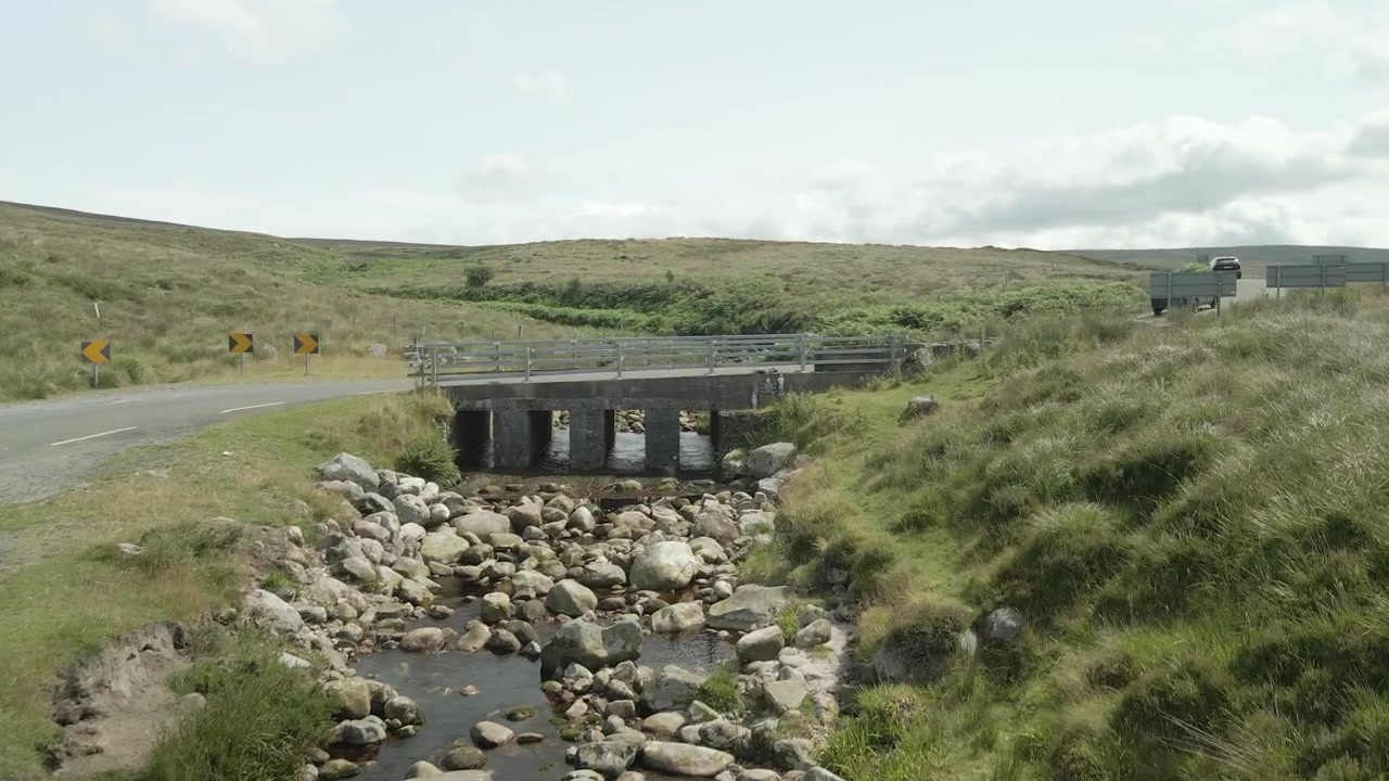 Un'auto attraversa un piccolo ponte di pietra su un ruscello nelle montagne di Wicklow in Irlanda in una giornata nuvolosa.