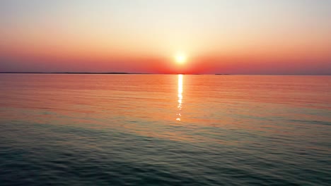 Rechts-Fliegende-Drohnenansicht-Des-Wunderschönen-Sonnenaufgangs-Am-Meer-Mit-Hell-Leuchtender-Sonne,-Die-Farbenfrohe-Rot-orange-violette-Und-Gelbe-Reflexe-über-Friedliche,-Plätschernde-Wellen-Des-Meeres-Mit-Wunderschönem-Himmel-Und-Wasser-Wirft