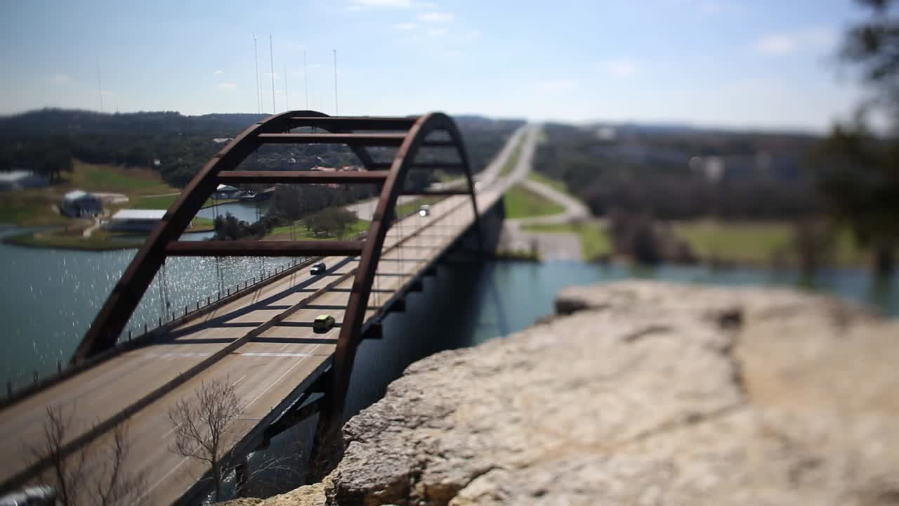 Austin Pennybacker Bridge  tilt-shifted time-lapse, focus tilted to highlight narrow segment of ledge - front part of bridge. Traffic is heavy on north side, it slows down but never fully stops.