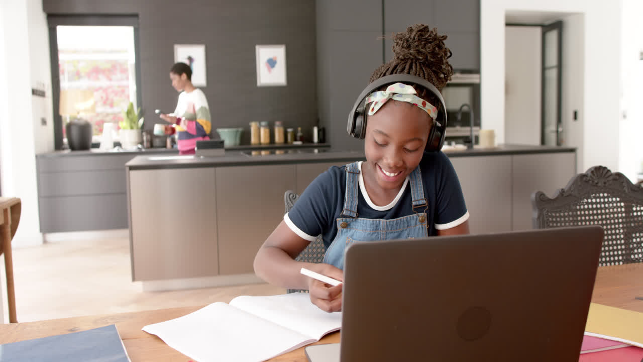 chica afroamericana feliz en clase en línea usando auriculares y portátil en cámara lenta