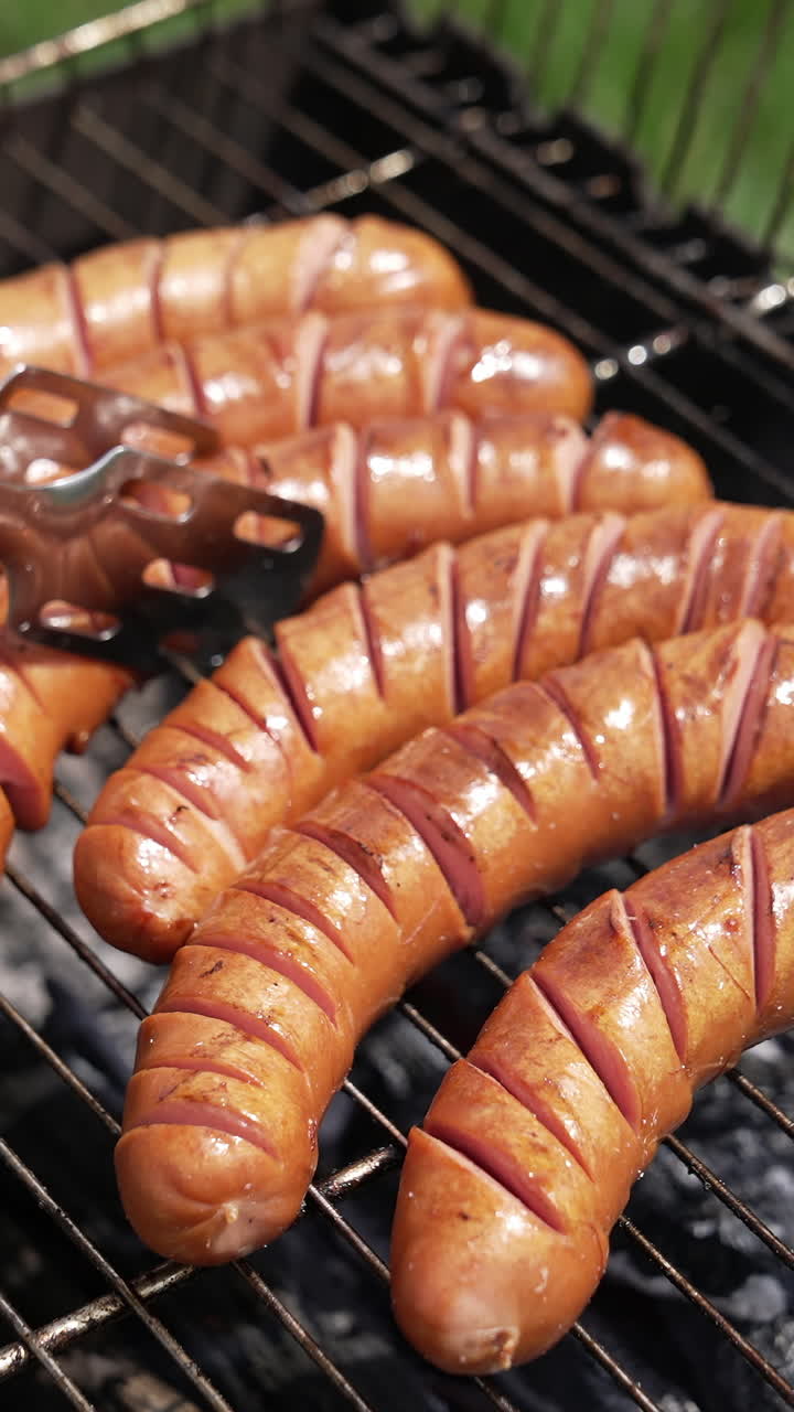 Cooking sausages in smoke outdoors. Tasty roast food on charcoal for picnic. Chef cooking grilled beef hot dog sausage on grill. Close-up. Vertical video