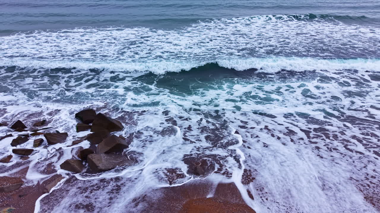 Le onde si infrangono su una costa rocciosa in un pomeriggio nuvoloso, sulla spiaggia vicino all'oceano.