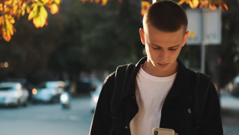 Joven-Estudiante-Caminando-Y-Usando-Teléfono-Móvil-Al-Aire-Libre.