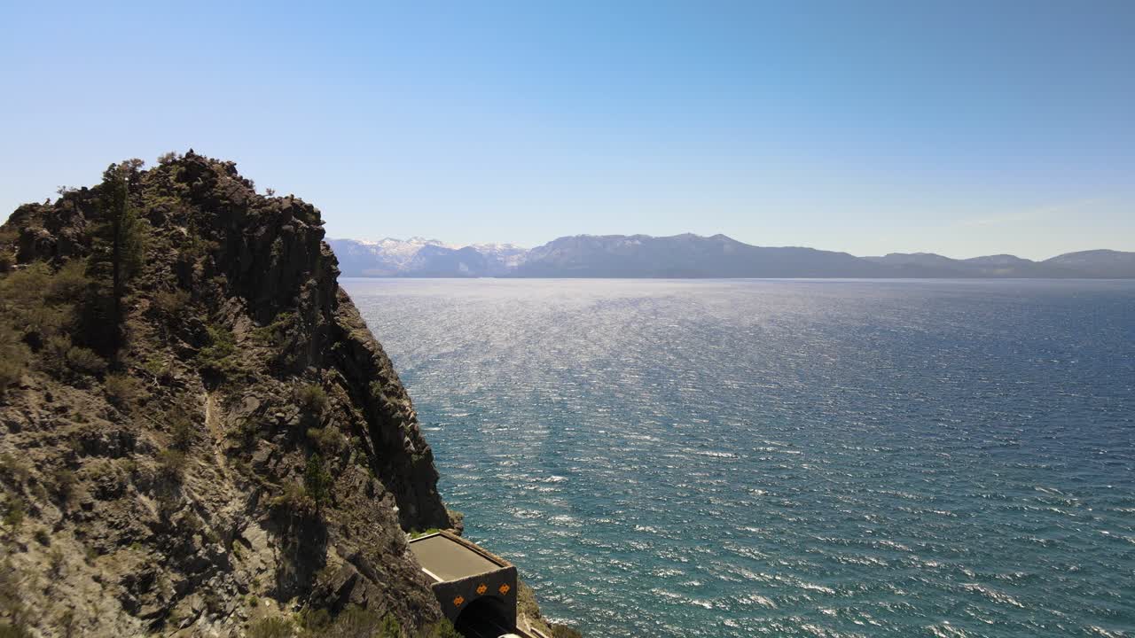 drone volando desde detrás de la roca de la cueva para luego revelar todo el lago tahoe y una extensión montañosa a lo largo del horizonte en el lado nevada del lago tahoe